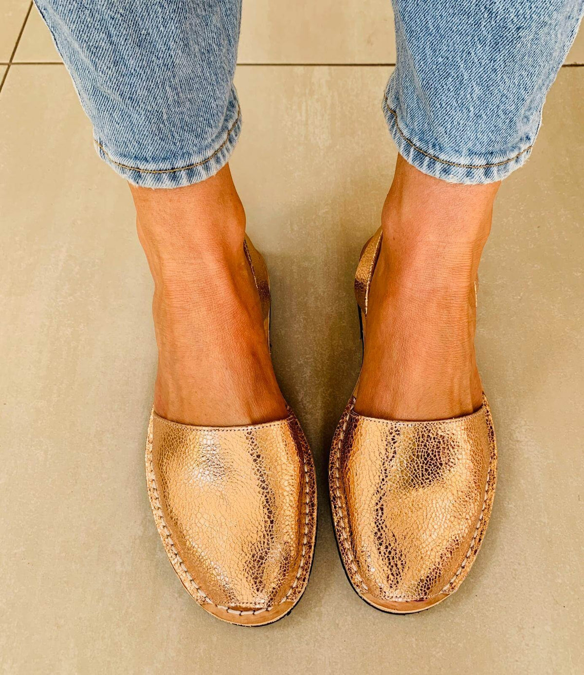 Rose Gold sandals worn with light blue jeans on a neutral background