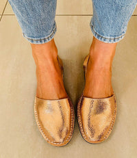 Rose Gold sandals worn with light blue jeans on a neutral background