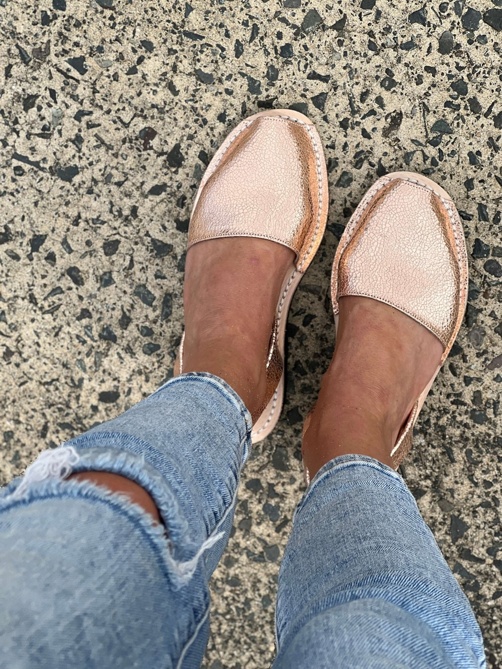 Rose gold avarcas worn with blue jeans on a textured pavement.