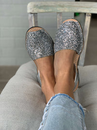Silver glittery sandals worn with light blue jeans on a chair.