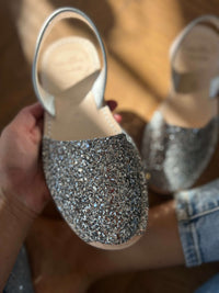 Silver glittery shoes held by a person with a blurred background