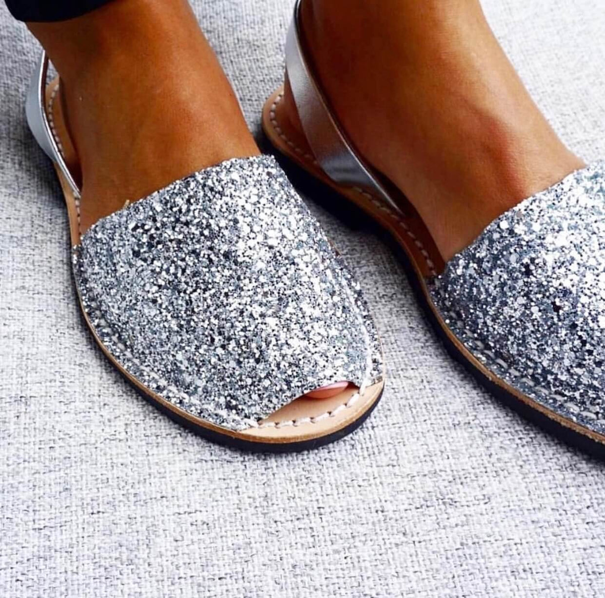 Silver glittery open-toe sandals on a textured surface