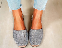 Silver glittery avarcas worn with light blue jeans on a neutral background