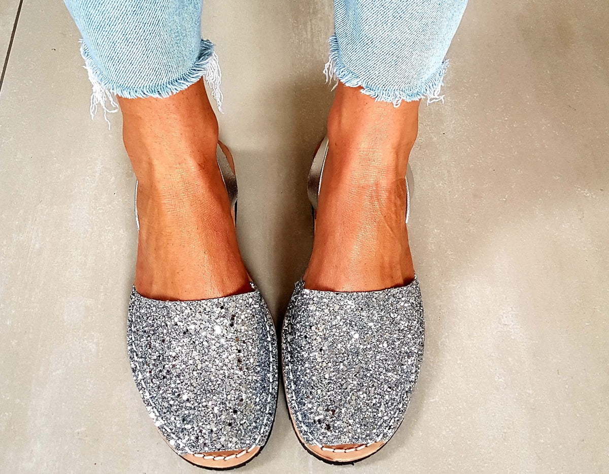 Silver glittery loafers worn with light blue jeans on a neutral background