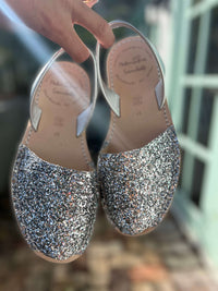 Pair of glittery silver shoes held by a hand with a blurred background