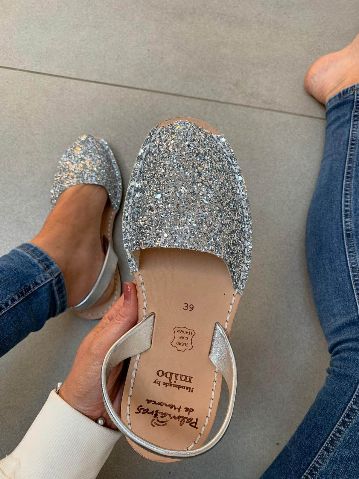 Silver glittery avarcas worn with jeans on a neutral background