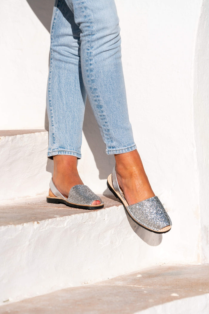 Person wearing light blue jeans and silver glittery avarcas on a white background