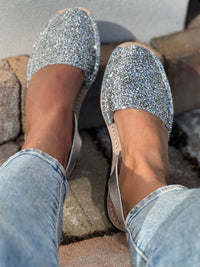 Silver glittery flats worn with light blue jeans on a stone surface