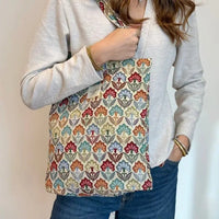Person holding a colorful floral-patterned bag against a plain background