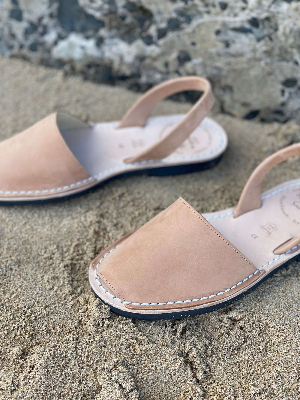 Pair of sandals on a sandy surface with a natural stone background