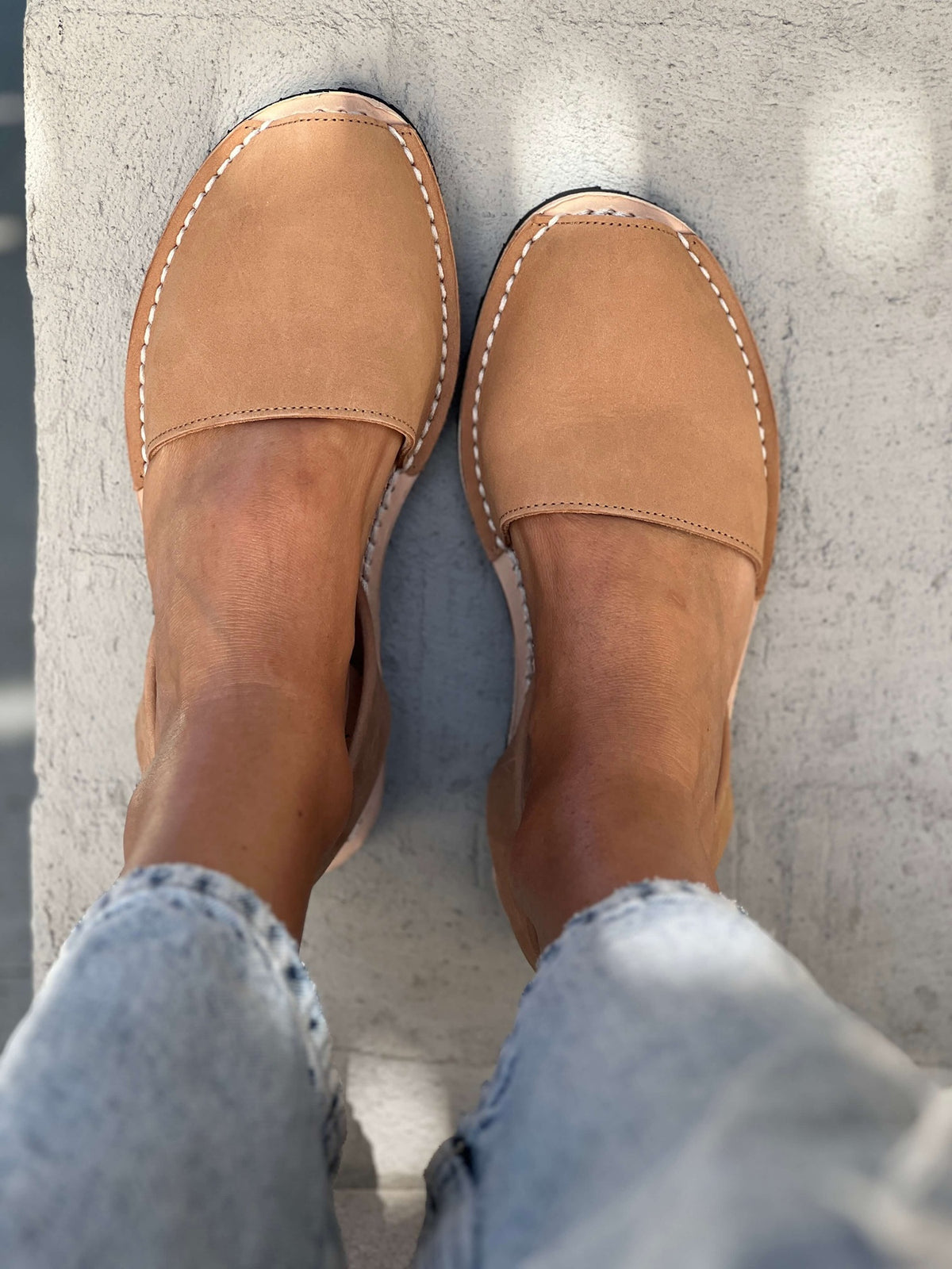 Tan nubuck leather shoes worn with light blue jeans on a concrete floor.