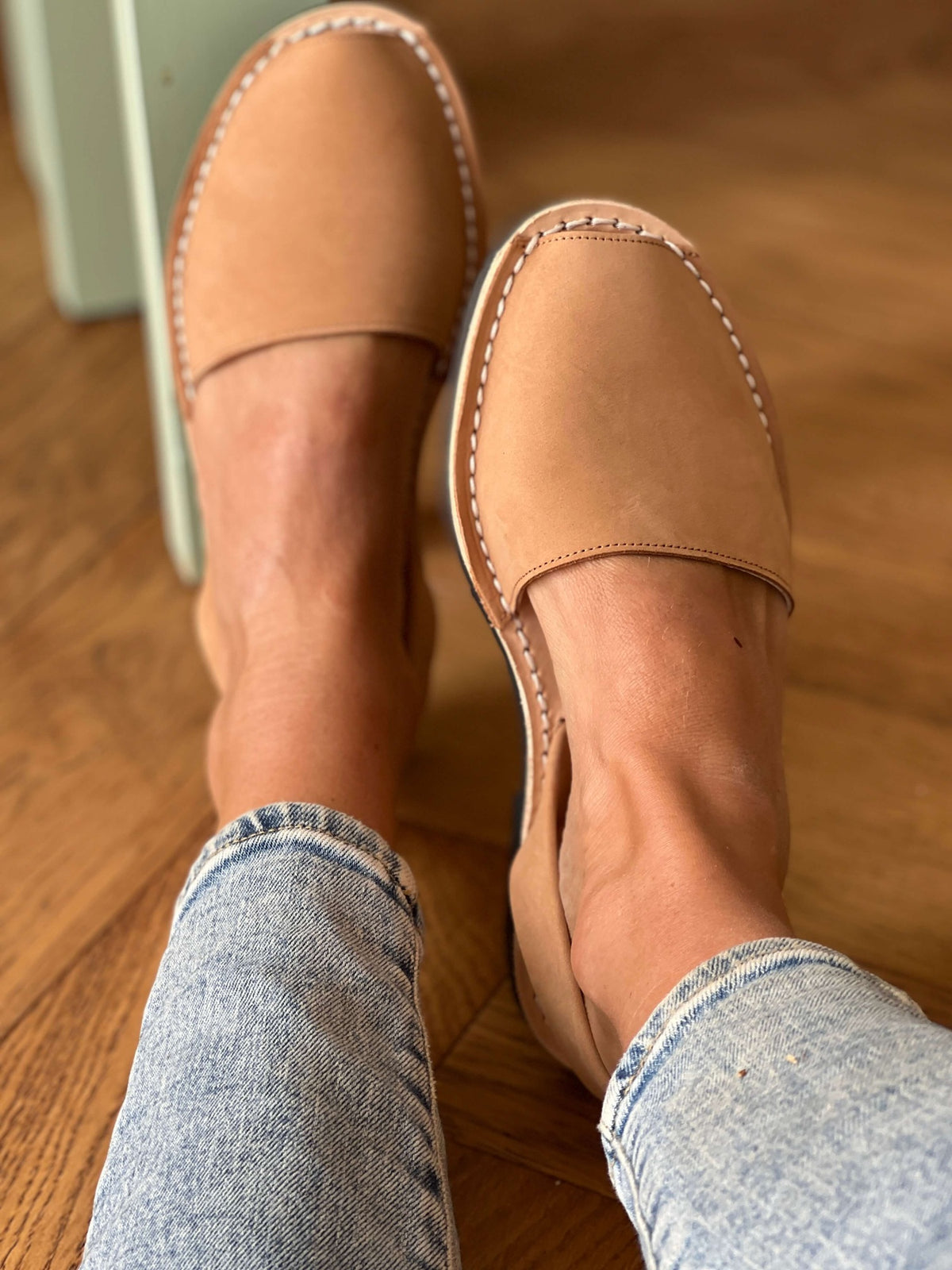 Tan avarcas worn with light blue jeans on a wooden floor.