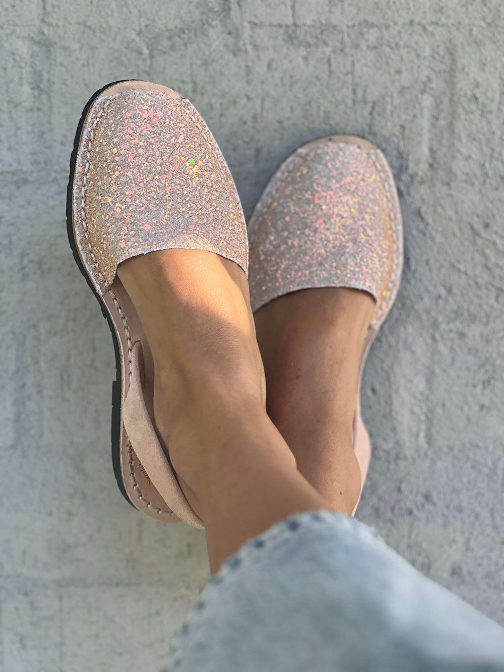 Pair of glittery pink shoes worn by a person against a grey concrete wall.