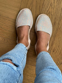 Person wearing sparkly avarcas and light blue jeans on a wooden floor.