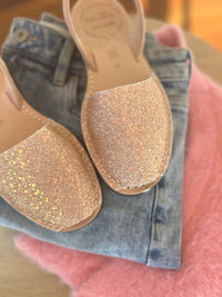 Glittery sandals on a pink surface with denim fabric in the background