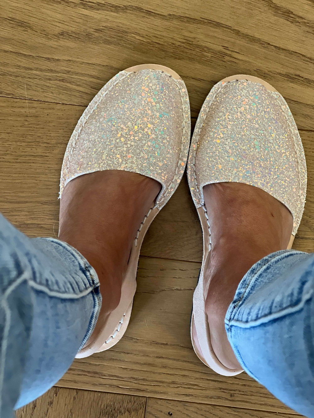 Pair of glittery shoes on a wooden floor with denim jeans.
