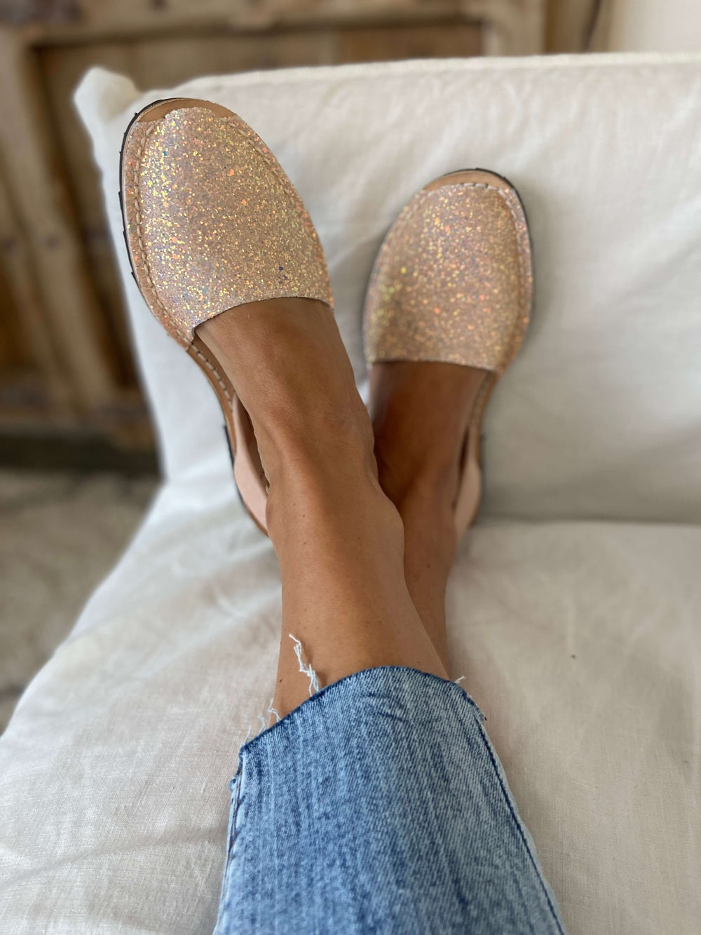 Person wearing sparkly shoes and blue jeans sitting on a white couch.