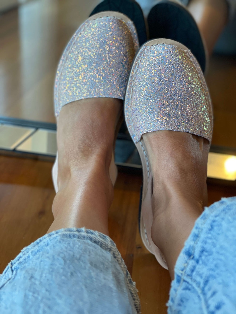 Silver glittery shoes worn indoors on a wooden floor.
